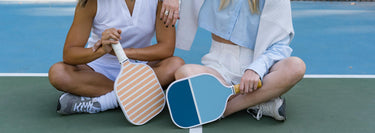 Two women sitting on pickleball court with GAMMA pickleball paddles